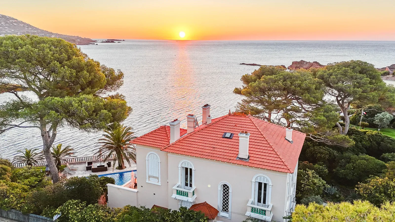 Villa de bord de mer au toit de tuiles rouges entourée de pins, face à la mer au coucher du soleil